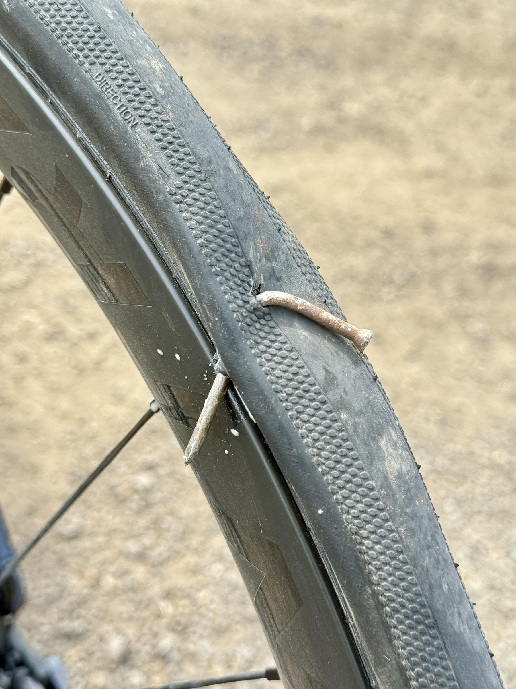 Photo of a bike tire with a nail sticking through it.